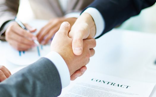 Image of business partners handshaking over business objects on workplace